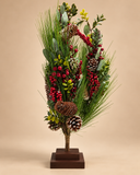 Mini árvore de Natal Campestre de 59 cm, com ramos de pinheiro, folhagens verdes, pinhas e cachos de frutinhas vermelhas, sobre base quadrada marrom em dois níveis, em fundo bege.