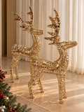 Rena decorativa de Natal Golden Reindeer com mosaico espelhado dourado, em estrutura aramada, sobre piso claro diante de cortina branca, ao lado de galhos de pinheiro com frutinhas vermelhas.