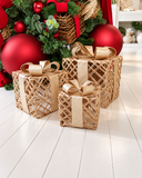 Caixas decorativas de Natal Trama Dourada em formato de presente, com trama vazada em tom natural e laço dourado, para decorar os pés da árvore.