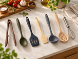 Jogo de utensílios de cozinha em silicone com 7 peças em cores sortidas (pegador, colher, espátula vazada, espátula, concha, escumadeira e fouet) sobre bancada de mármore com temperos.