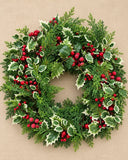 Guirlanda de Natal Boas-Vindas com 60 cm de diâmetro, com ramos verdes de cipreste e pinheiro, folhas de azevinho rajadas em verde e creme e cachos de frutinhas vermelhas.