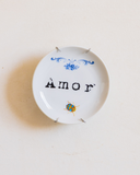 Vista frontal do prato decorativo Pequeno Amor em porcelana com besouro azul e dourado, pendurado na parede