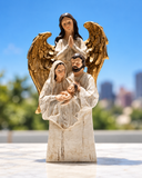 Escultura decorativa Proteção Família em resina off-white, com a Sagrada Família e um anjo de asas douradas, sobre fundo de céu azul e cidade desfocada.