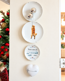 Composição de parede com pratos decorativos e o coração Compasso do Amor em porcelana, ao lado de árvore de Natal